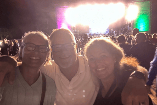 3 dunkle Gestalten stehen vor einer beleuchteten Bühne